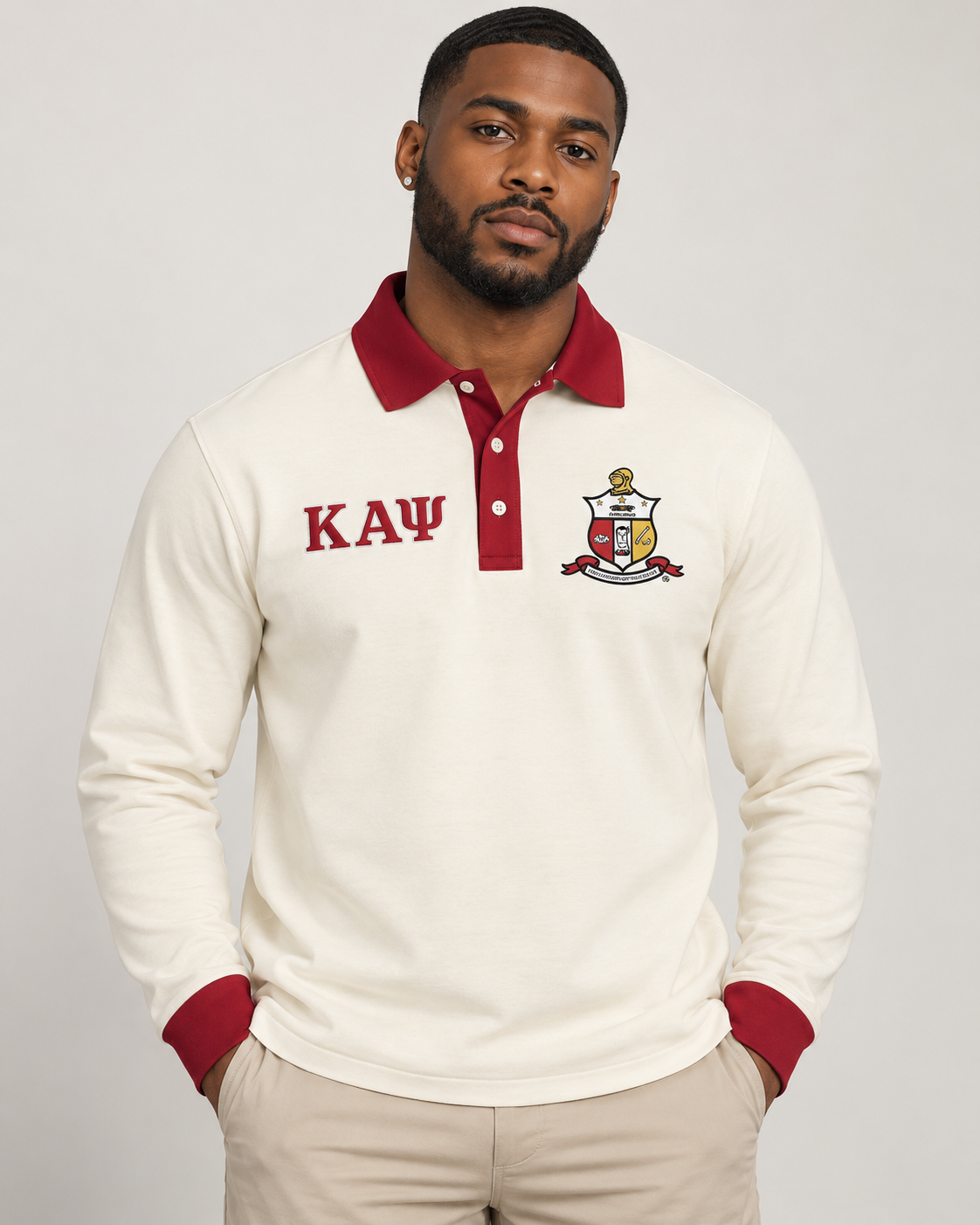 Kappa Alpha Psi man wearing cream long-sleeve polo with crimson collar, placket, cuffs, crest, and Greek letters