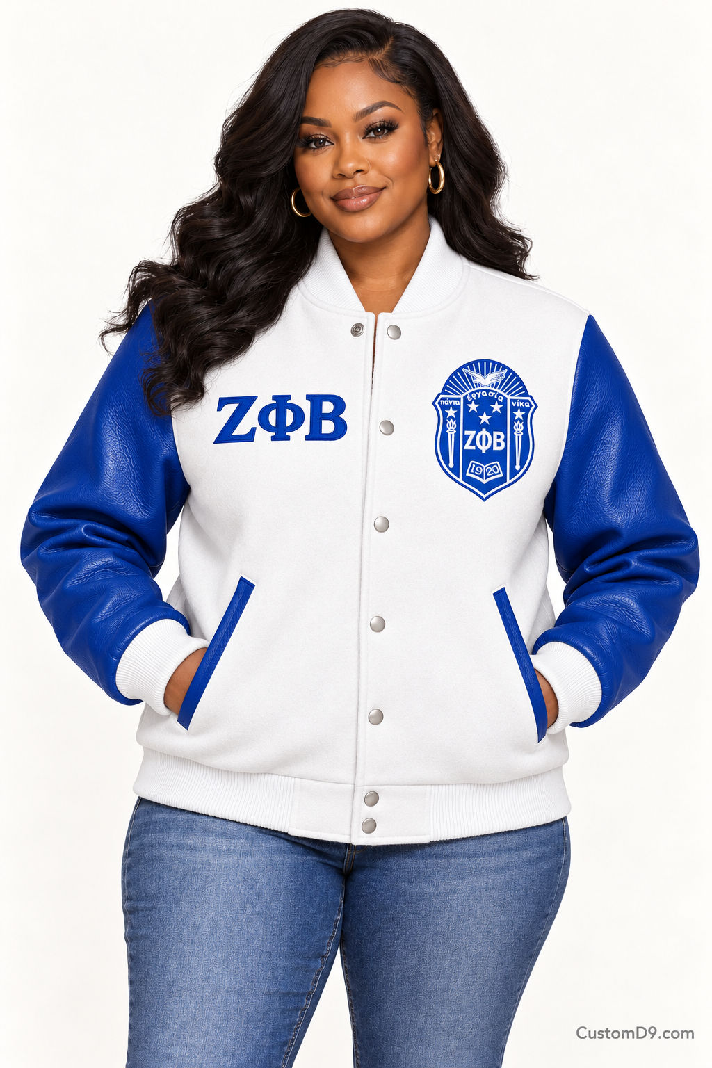 Black woman modeling Zeta Phi Beta white body and royal blue sleeve premium varsity jacket, front view; horizontal Greek letters on right chest and crest on left chest.