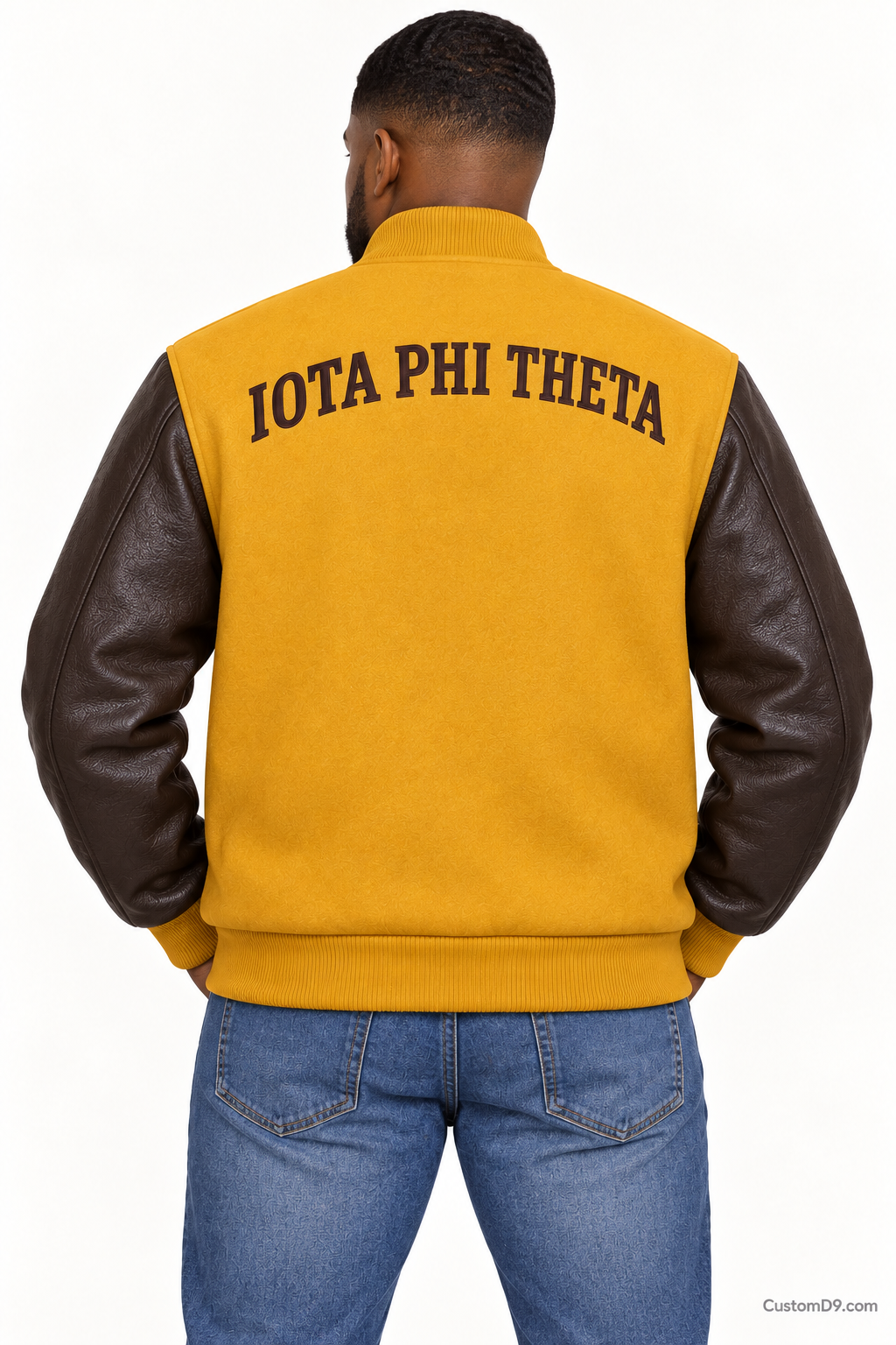 Black man modeling Iota Phi Theta premium contrast varsity jacket with gilded gold body and charcoal brown sleeves, back view.