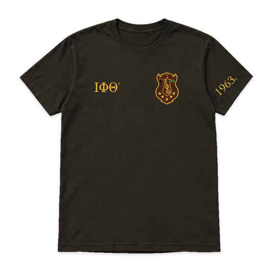 Digital product mockup: Iota Phi Theta charcoal brown T-shirt with original brand-kit shield on wearer's left chest, small gold Greek letters and 1963 on wearer's left sleeve