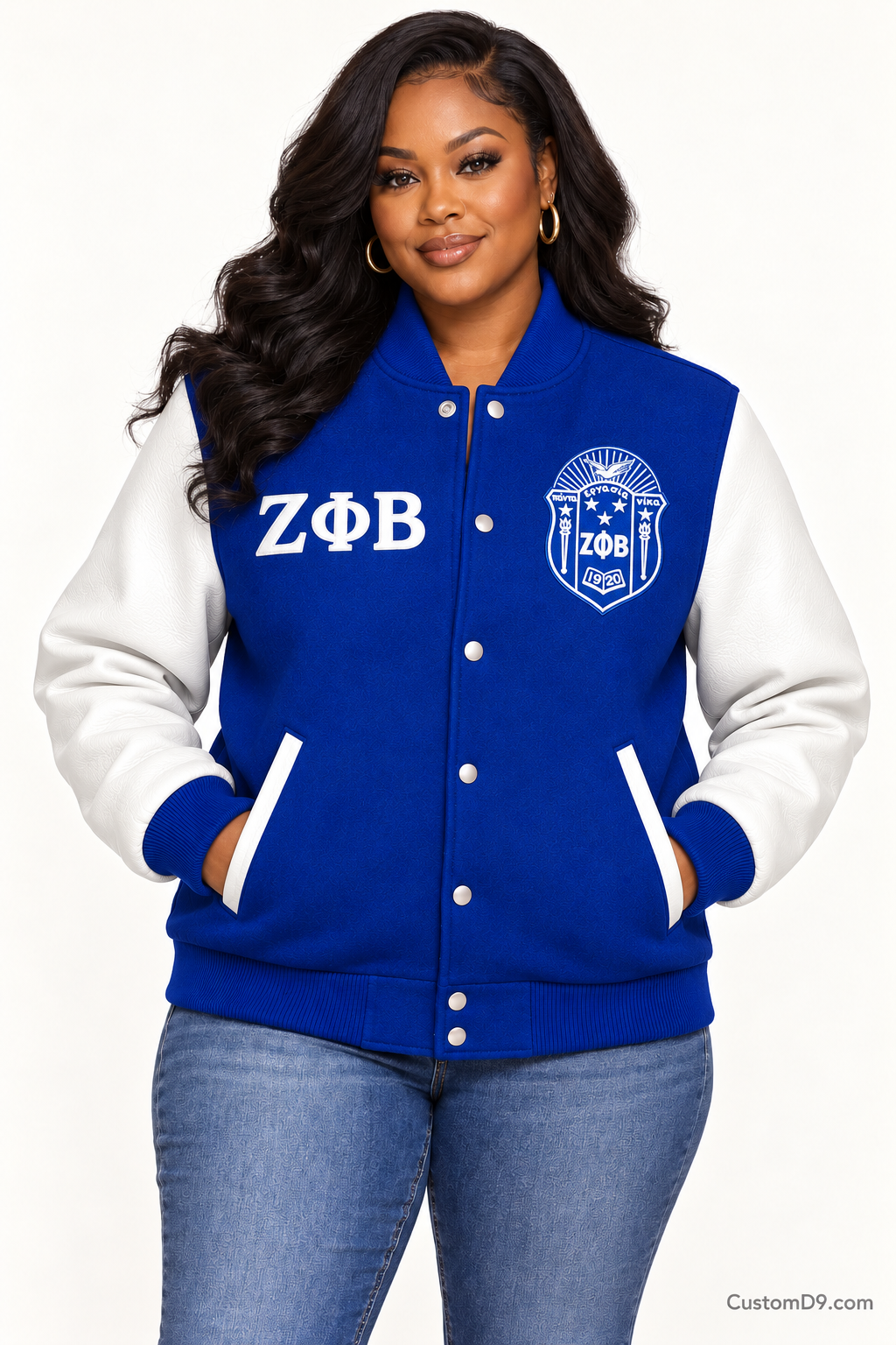 Black woman modeling Zeta Phi Beta royal blue body and white sleeve premium varsity jacket, front view; horizontal Greek letters on right chest and crest on left chest.