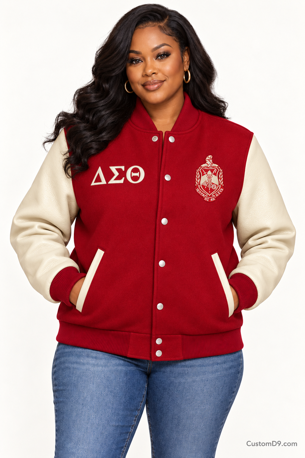 Black woman modeling Delta Sigma Theta crimson body and cream sleeve premium varsity jacket, front view; horizontal Greek letters on right chest and crest on left chest.