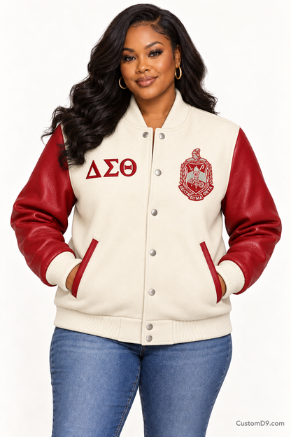 Black woman modeling Delta Sigma Theta cream body and crimson sleeve premium varsity jacket, front view; horizontal Greek letters on right chest and crest on left chest.