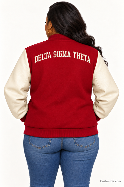 Black woman modeling Delta Sigma Theta crimson body and cream sleeve premium varsity jacket, back view; arched organization name across upper back.