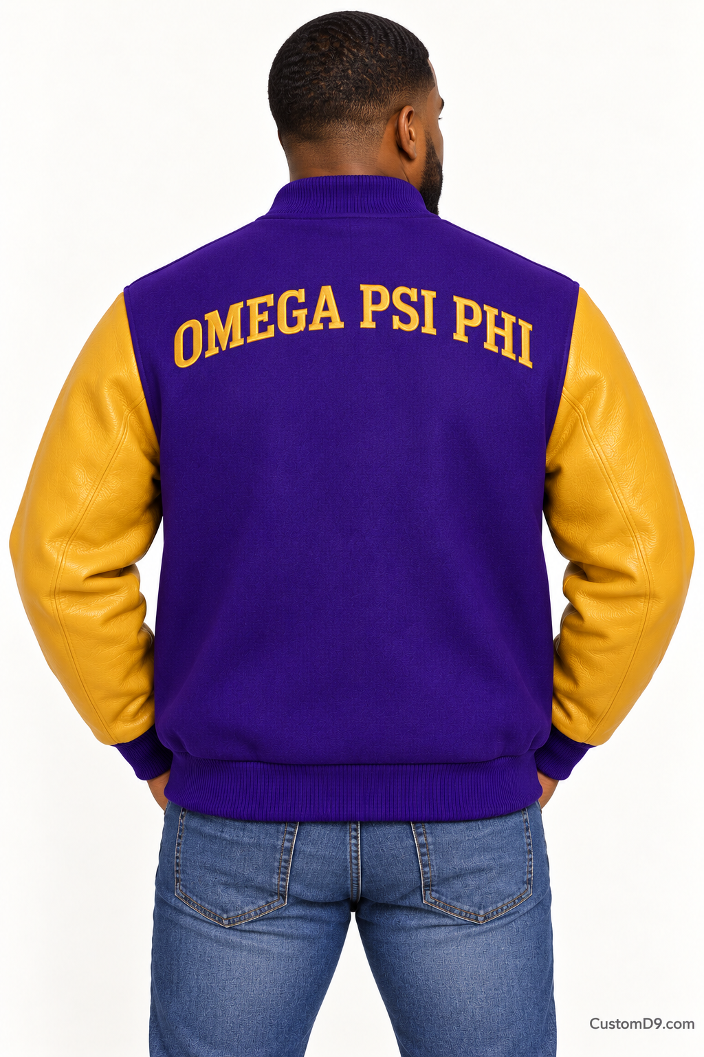 Black man modeling Omega Psi Phi premium contrast varsity jacket with royal purple body and old gold sleeves, back view.