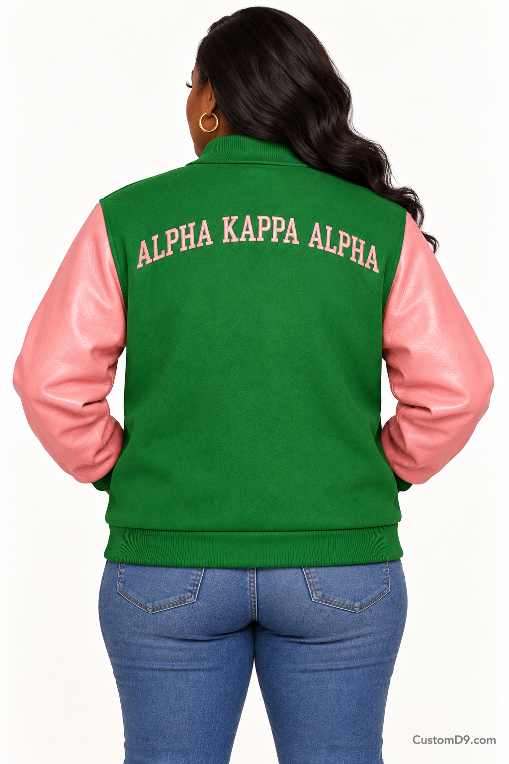 Black woman modeling Alpha Kappa Alpha apple green body and salmon pink sleeve premium varsity jacket, back view; arched organization name across upper back.